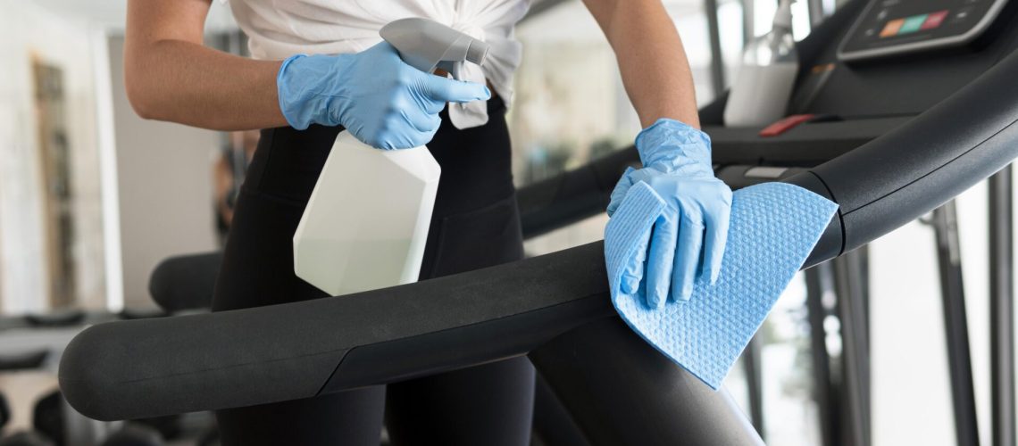 woman-with-gloves-cleaning-solution-disinfecting-gym-equipment